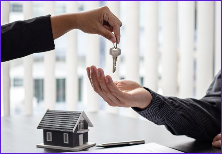 Person handing over house keys with small model home on desk — symbolizing a successful conventional mortgage closing in Smyrna, GA.